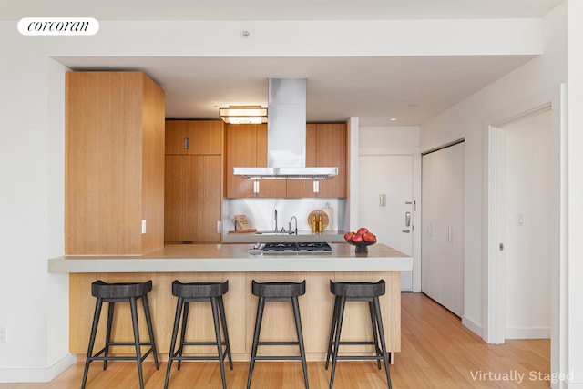 450 W 17th St Unit 2408, New York City, NY 10011 - kitchen with wall chimney exhaust hood, a breakfast bar, modern cabinets, and brown cabinets
