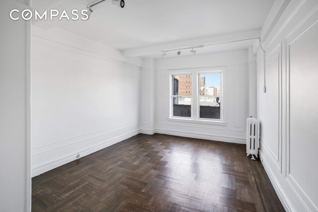 unfurnished room featuring radiator and rail lighting