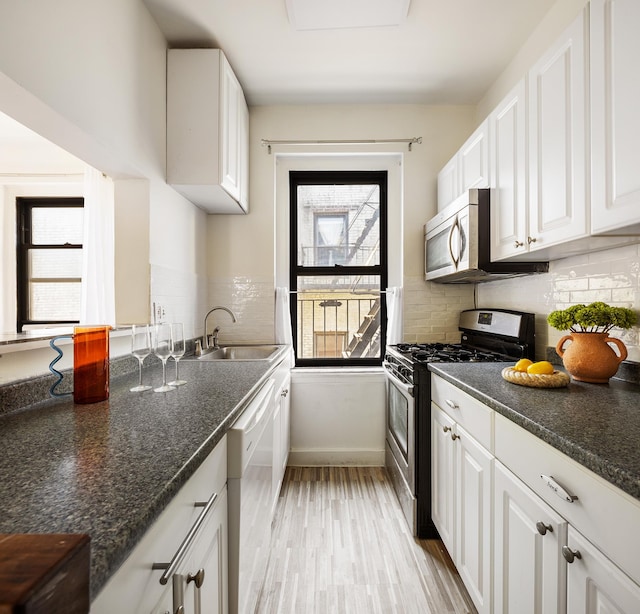 kitchen with appliances with stainless steel finishes, baseboards, white cabinets, and a sink
