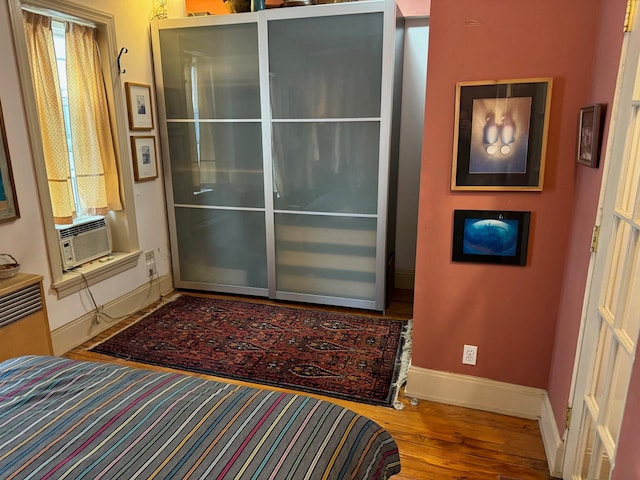 bedroom with cooling unit, wood finished floors, and baseboards
