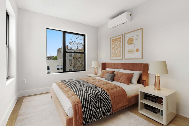 bedroom featuring baseboards, light wood finished floors, and a wall mounted air conditioner