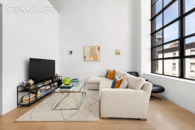 living area with a high ceiling, light wood-style flooring, and baseboards