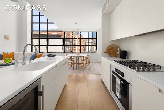 kitchen featuring a sink, appliances with stainless steel finishes, white cabinets, wine cooler, and light wood-style floors