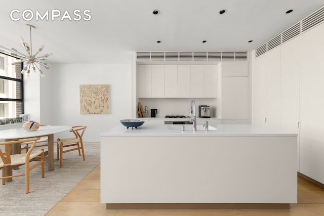kitchen with a sink, a chandelier, a center island with sink, white cabinetry, and light countertops