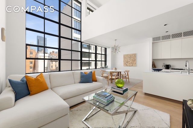 living room featuring a chandelier, light wood-type flooring, a high ceiling, and a city view
