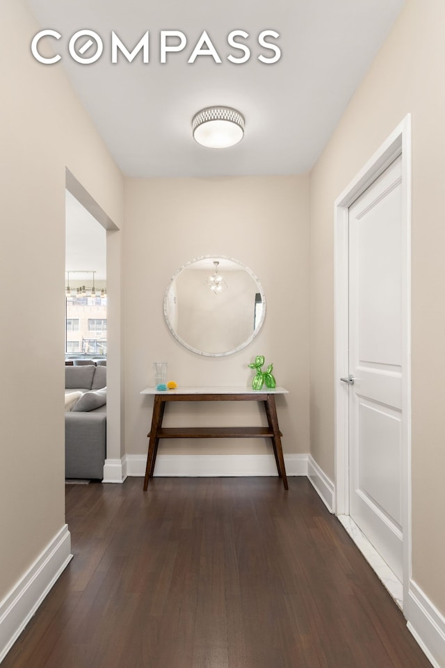 hall with wood finished floors, baseboards, and a chandelier