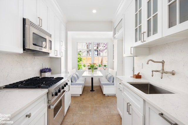 kitchen featuring stone tile flooring, white cabinets, tasteful backsplash, a sink, and appliances with stainless steel finishes