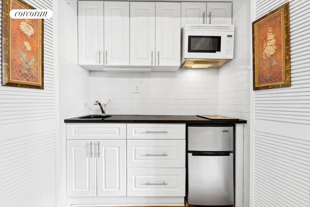 45 Tudor City Pl Unit 808, New York City, NY 10017 - kitchen with freestanding refrigerator, white microwave, dark countertops, decorative backsplash, and white cabinets