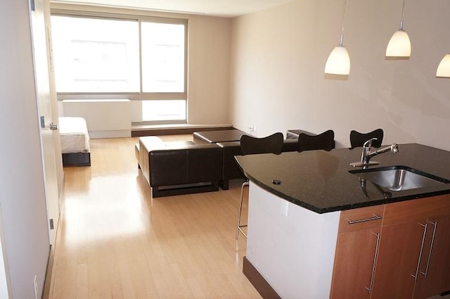 kitchen featuring decorative light fixtures, light wood-style floors, brown cabinets, and a sink