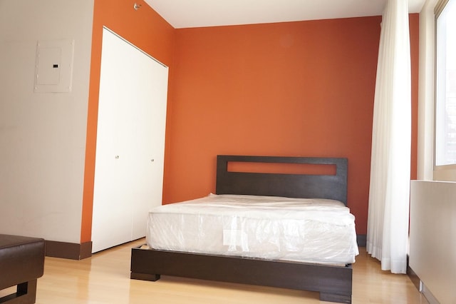 bedroom featuring wood finished floors, a closet, electric panel, and multiple windows