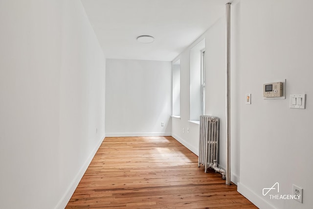 corridor with radiator, wood finished floors, and baseboards