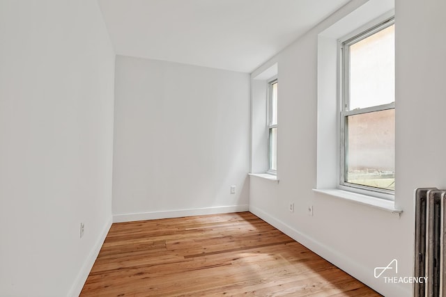 unfurnished room featuring radiator, light wood-style floors, and baseboards