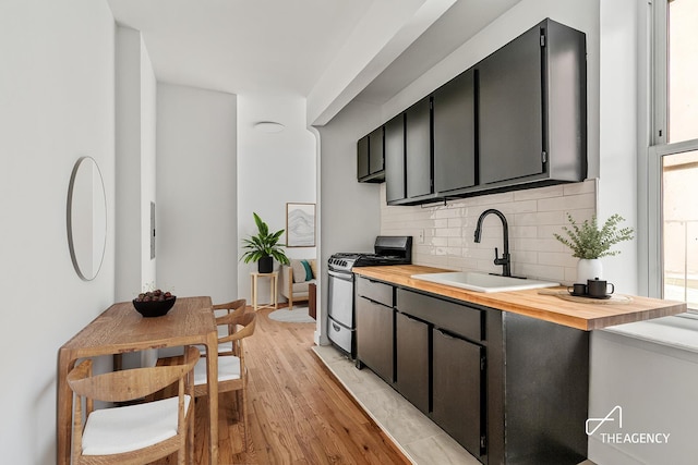 kitchen featuring stainless steel range with gas cooktop, a sink, tasteful backsplash, light wood finished floors, and butcher block counters