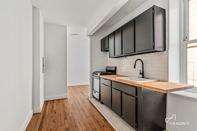 kitchen with stainless steel gas range oven, a sink, wooden counters, backsplash, and baseboards