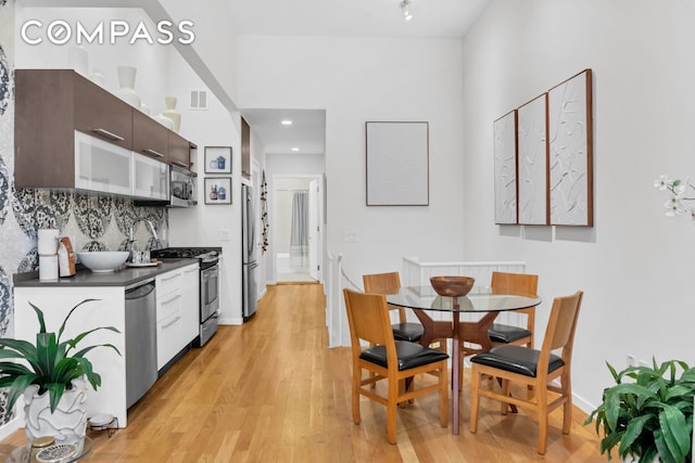 kitchen with dark countertops, light wood-style floors, stainless steel appliances, decorative backsplash, and visible vents