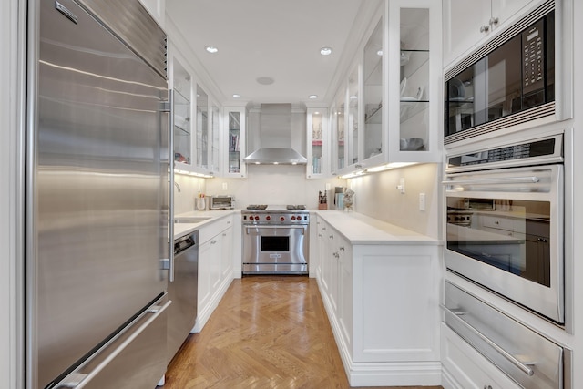 kitchen featuring light countertops, white cabinetry, wall chimney range hood, and built in appliances
