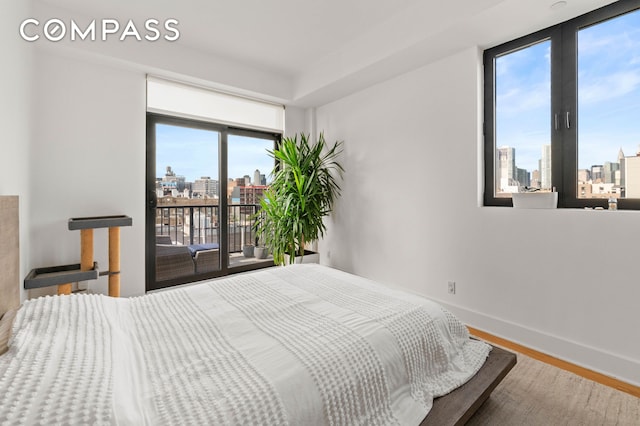 bedroom featuring baseboards, a city view, wood finished floors, and access to exterior