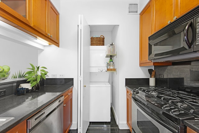 kitchen with visible vents, stacked washer and dryer, dark stone countertops, and appliances with stainless steel finishes