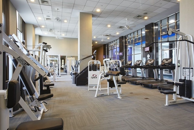 workout area featuring carpet floors, visible vents, a drop ceiling, and a towering ceiling
