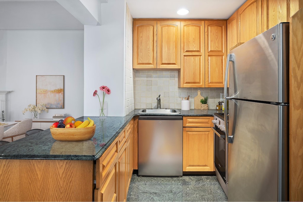kitchen with a sink, decorative backsplash, dark stone countertops, a peninsula, and appliances with stainless steel finishes