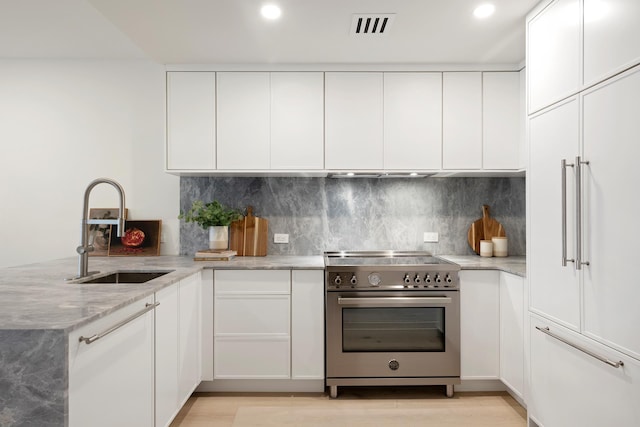 kitchen featuring a peninsula, high end stainless steel range, light stone countertops, white cabinets, and a sink