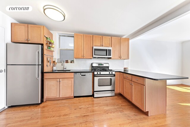 203 W 122nd St Unit 4, New York City, NY 10027 - kitchen featuring appliances with stainless steel finishes, a sink, a peninsula, light wood-style flooring, and dark countertops