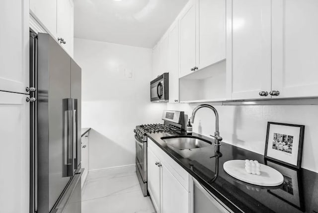 kitchen with dark stone counters, white cabinetry, a sink, appliances with stainless steel finishes, and baseboards