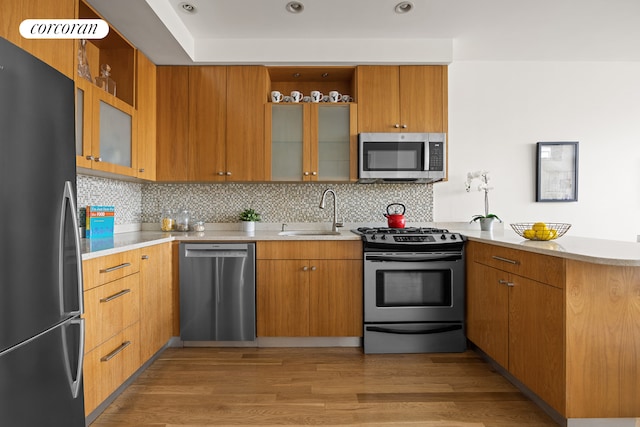 kitchen featuring a sink, light wood-style floors, light countertops, stainless steel appliances, and a peninsula