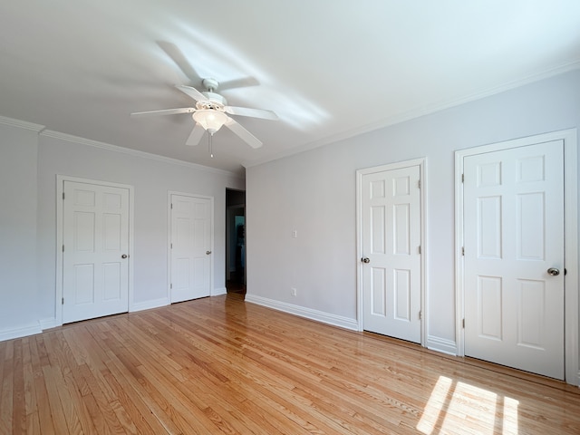 unfurnished bedroom featuring baseboards, ornamental molding, two closets, and light wood-style flooring