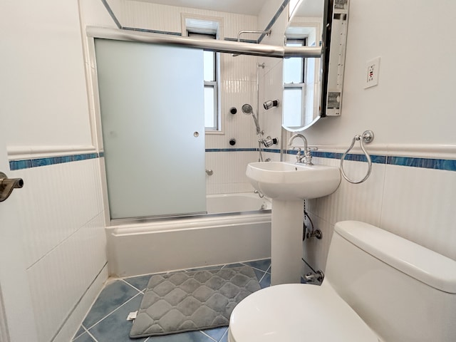 bathroom with wainscoting, toilet, tile patterned floors, enclosed tub / shower combo, and tile walls