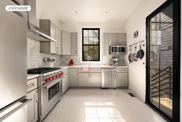 kitchen featuring visible vents, gray cabinetry, light countertops, stainless steel appliances, and wall chimney exhaust hood