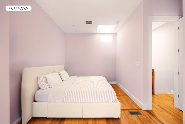 bedroom with baseboards, a skylight, visible vents, and wood finished floors