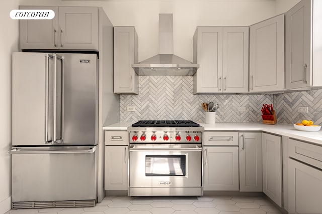 kitchen featuring light countertops, gray cabinetry, high end appliances, and wall chimney exhaust hood