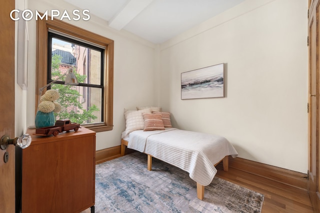 bedroom with baseboards, wood finished floors, and beam ceiling