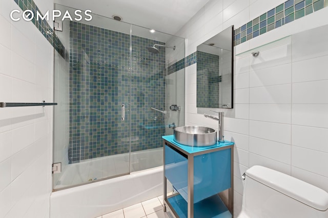full bath featuring vanity, bath / shower combo with glass door, toilet, and tile walls