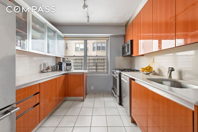 kitchen with brown cabinets, rail lighting, a sink, light countertops, and stainless steel appliances