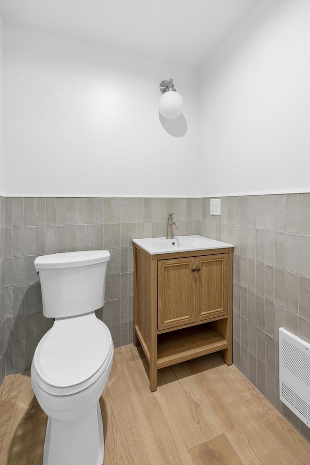 half bath featuring vanity, toilet, a wainscoted wall, tile walls, and heating unit
