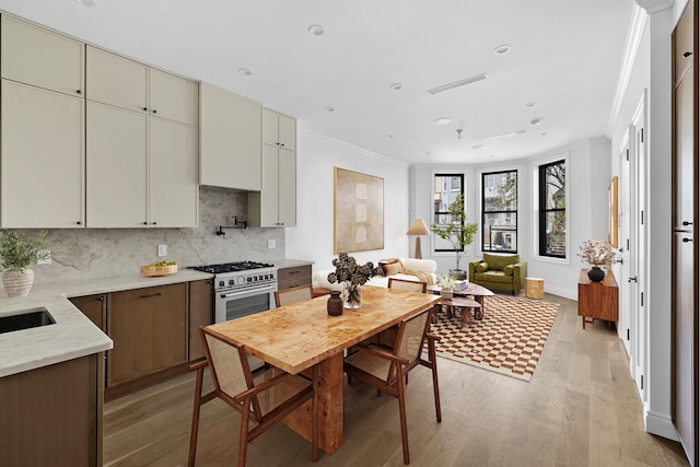 kitchen featuring ornamental molding, baseboards, tasteful backsplash, light wood-style flooring, and stainless steel range