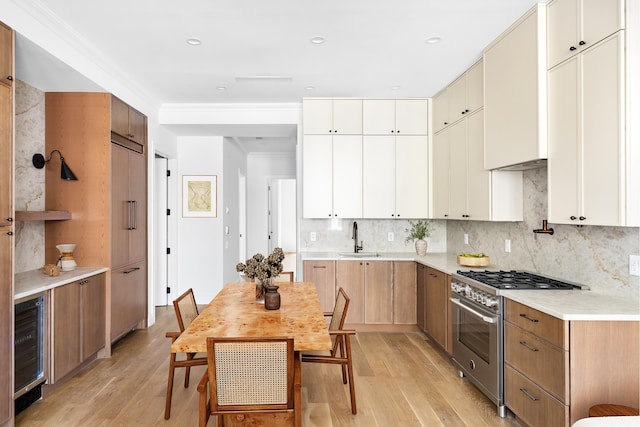 kitchen with a sink, beverage cooler, light wood-style flooring, backsplash, and high end stainless steel range oven