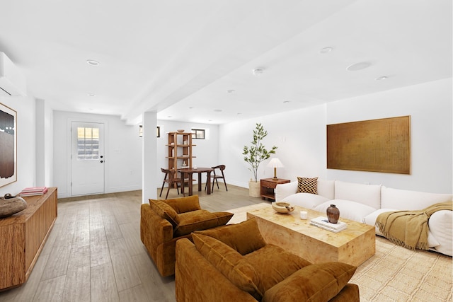living room with an AC wall unit, baseboards, and light wood finished floors