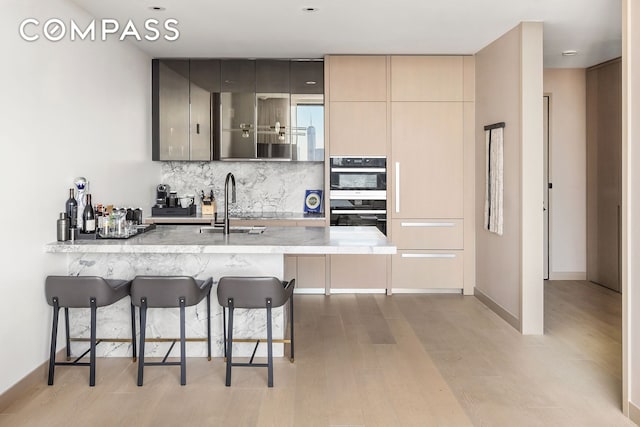 kitchen featuring a kitchen breakfast bar, multiple ovens, modern cabinets, and tasteful backsplash