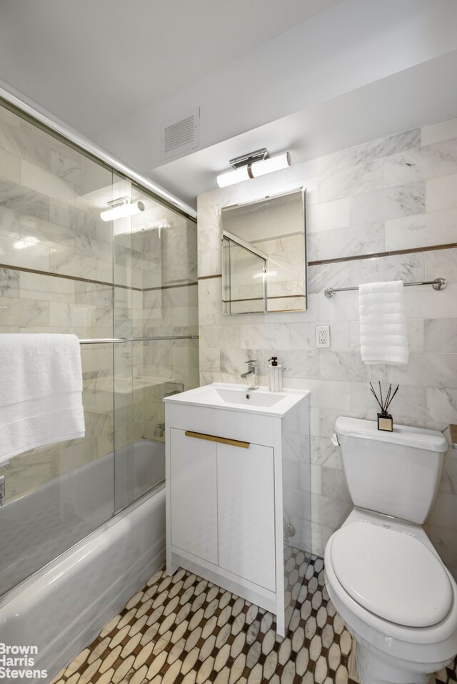 bathroom featuring visible vents, tile walls, vanity, toilet, and shower / bath combination with glass door