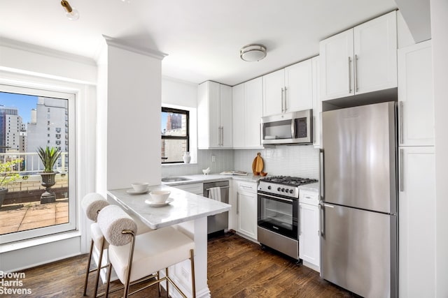 kitchen featuring decorative backsplash, a breakfast bar area, stainless steel appliances, and white cabinetry