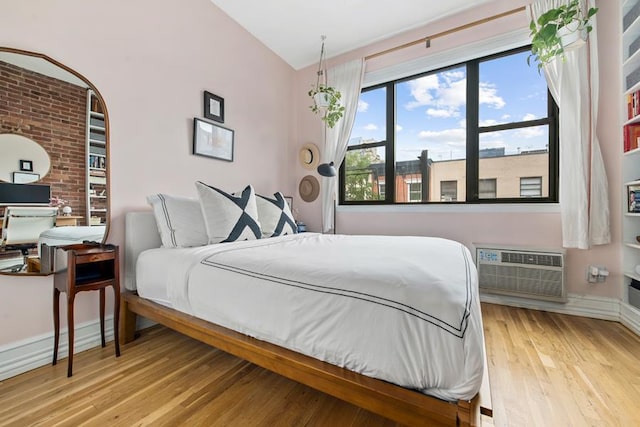bedroom featuring a wall mounted air conditioner, light wood finished floors, lofted ceiling, and baseboards