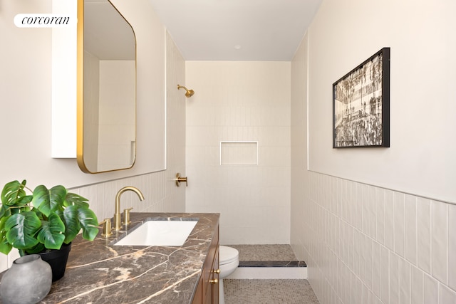 bathroom featuring vanity, wainscoting, a tile shower, and toilet