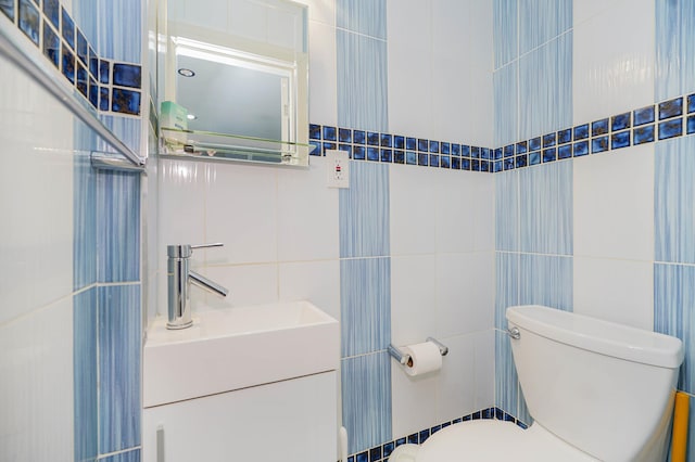 half bath with tile walls, toilet, and vanity
