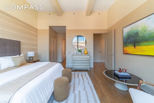 bedroom with baseboards, beamed ceiling, and wood finished floors