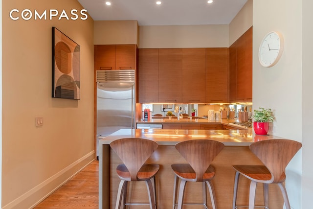 kitchen featuring stainless steel built in fridge, light countertops, a sink, a peninsula, and a breakfast bar