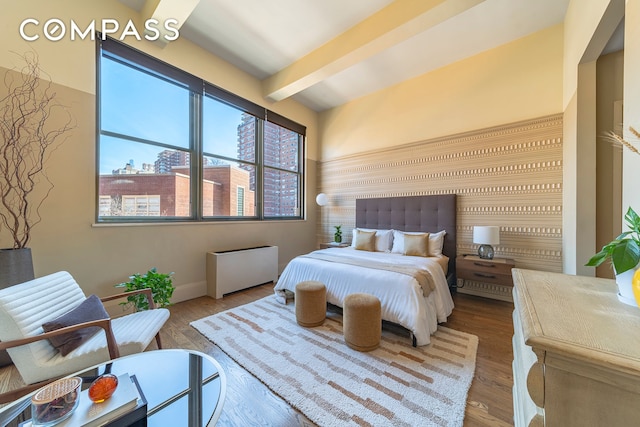 bedroom with a city view, wood finished floors, and beam ceiling