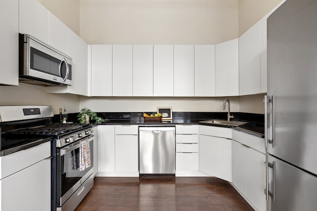 kitchen featuring stainless steel appliances, dark countertops, dark wood-type flooring, and a sink